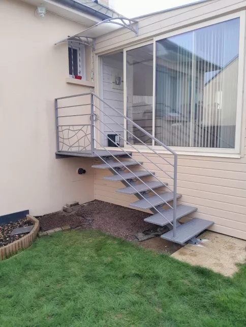 Escalier extérieur 6 marches + 1 palier. Marches en acier larmés. Garde corps en aluminium, cadre 40x20mm, remplissage en lisses D.16 + soubassement habillage décoratif "spline" sur le garde corps droit. 53810 CHANGE