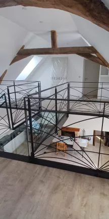 Escalier limon central 1/4 tournant débillardé, marches en chêne rustique sablé, laquage ral 2100 sablé Garde corps poteaux plats, remplissage lisses D.10 cintrées, main courante 40x10, laquage ral 2100 sablé Ossature en UPN, remplissage en dalle de verre clair, laquage de l'ossature ral noir 2100 sablé 72170 SEGRIE