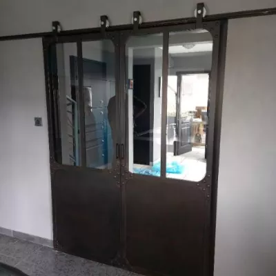 Porte verrière coulissante, châssis en acier 40mm,remplissage en vitrages clair 33/2 feuilleté, soubassement en tôle,roulettes apparentes, finition acier brut rouillé, 53600 EVRON.